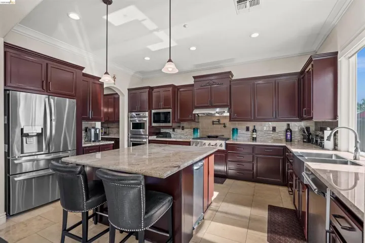 Gourmet kitchen featuring a large central island with granite countertop, dark wood cabinetry, stainless steel appliances, and tile flooring