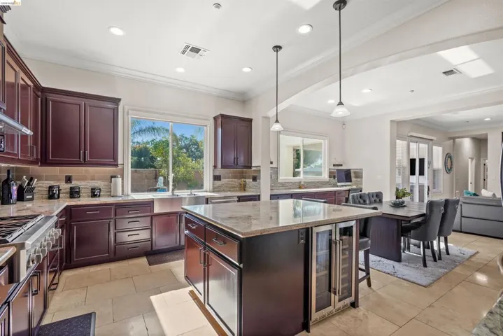 Open-concept kitchen featuring dark wood cabinetry, light-toned stone countertops, and a central island with integrated beverage coolers