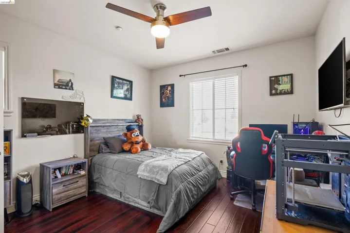 Bedroom featuring rich wood-finish flooring, a ceiling fan with integrated lighting, and a window with blinds