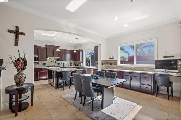Open-concept kitchen and dining area featuring warm wood cabinetry, a central island with bar seating, tile flooring, and ample natural light from exterior windows