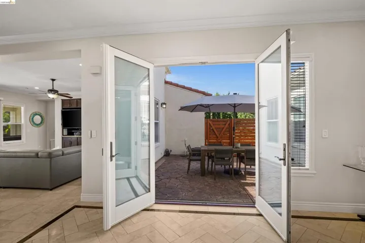 French doors opening to a private patio featuring stone paving and a wood privacy fence
