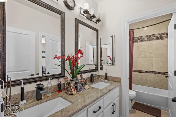 Bathroom featuring a dual vanity with granite-finish countertops, undermount sinks, and matte black fixtures