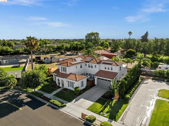 Two-story stucco residence featuring a tile roof, solar panels, an attached two-car garage, and a manicured front lawn with mature landscaping