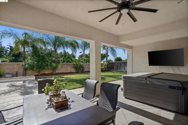 Covered patio with a ceiling fan, wall-mounted television, and a built-in spa