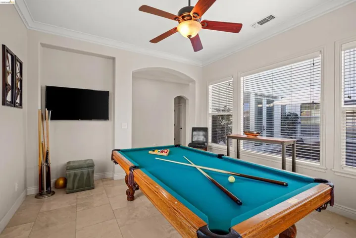 Spacious recreation area featuring neutral paint, crown molding, a ceiling fan with integrated lighting, and tile flooring