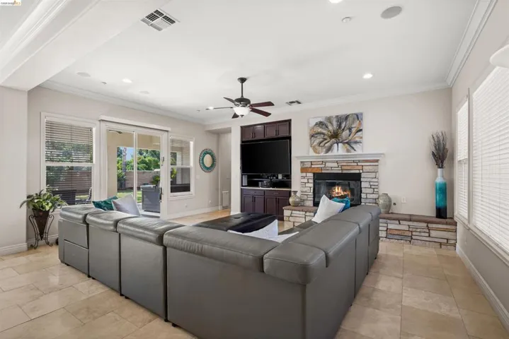 Spacious living area featuring tile flooring, a stone-clad fireplace with a hearth, a built-in entertainment center, a ceiling fan, and sliding glass doors opening to the outdoors