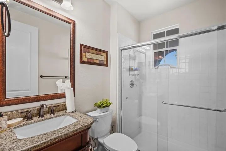 Bathroom featuring a granite-look countertop, undermount sink, bronze-tone faucet, and a shower with a sliding glass door