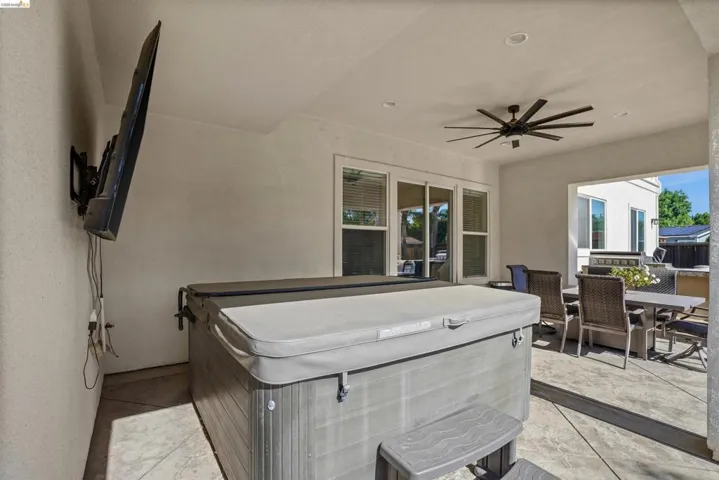 Covered patio featuring a hot tub with a protective cover and steps, mounted television, ceiling fan, and recessed lighting