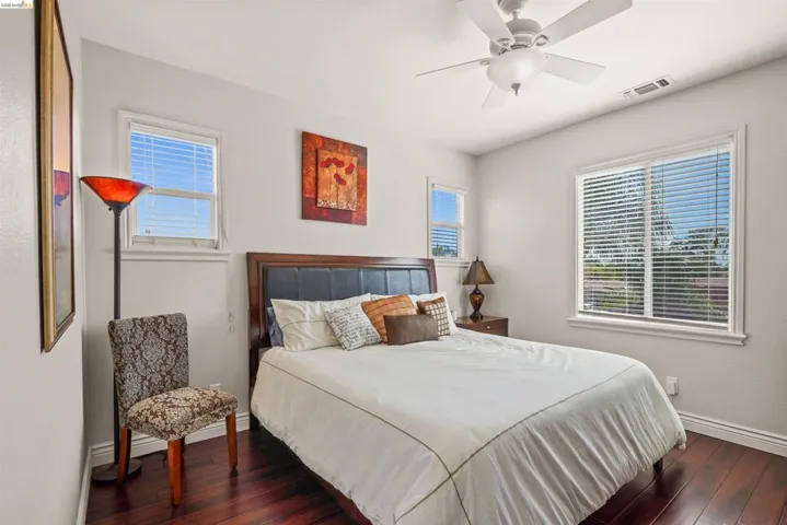 Bedroom featuring rich wood-finish flooring, white walls, and a ceiling fan