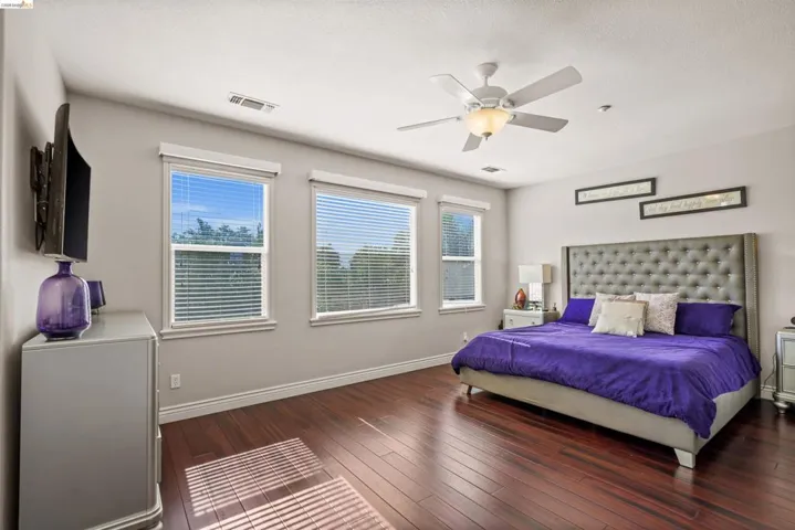 Spacious room featuring rich wood-finish flooring, multiple windows with blinds, and a ceiling fan with integrated lighting