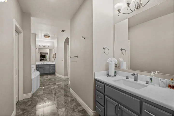 Bathroom featuring a grey vanity with a white countertop and rectangular undermount sink, brushed nickel faucet, large wall-mounted mirror, and overhead vanity lighting