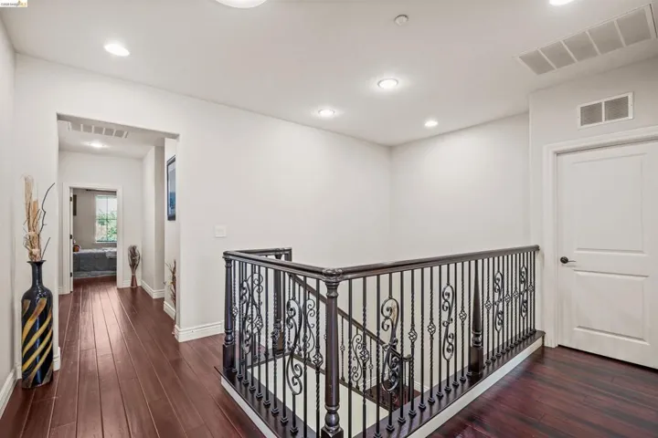 Upper floor landing featuring rich wood-finish flooring, recessed lighting, and a decorative wrought iron and wood staircase railing