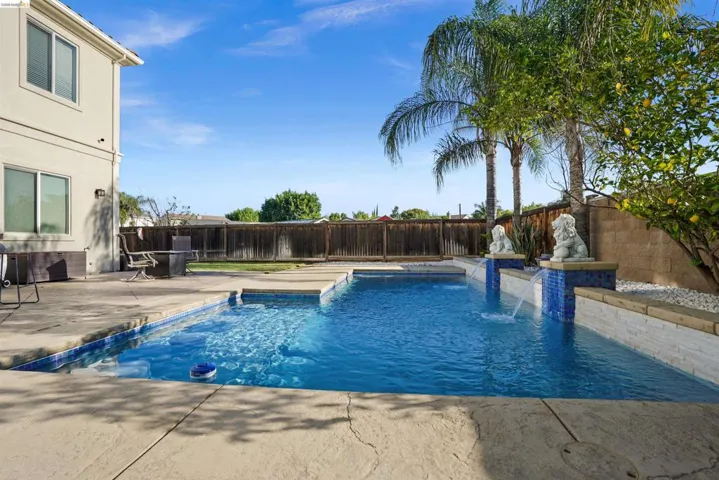 The backyard features a rectangular swimming pool with a concrete surround, accented by mosaic tile details and two water features