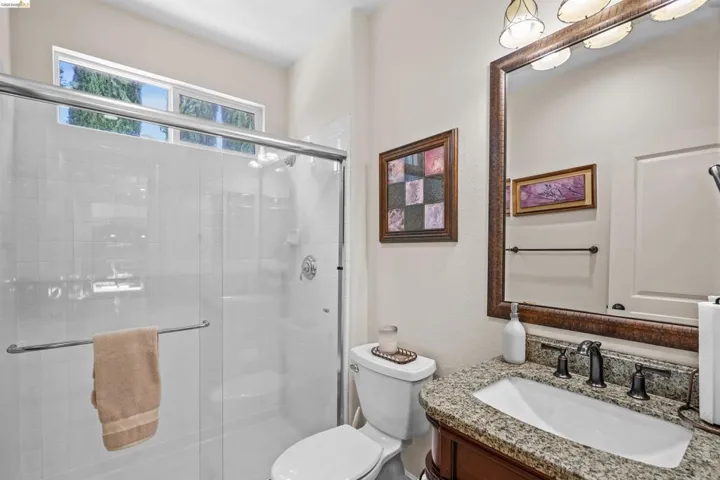 Bathroom featuring a glass-enclosed shower with white subway tile, a high transom window, a vanity with a granite countertop, and an ornate framed mirror with sconce lighting
