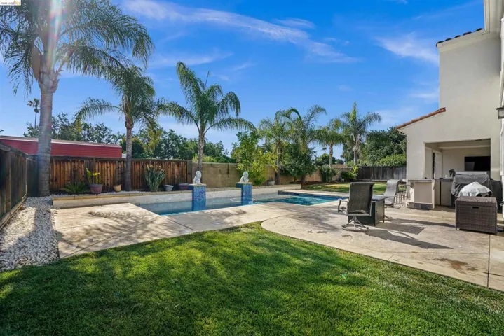 Outdoor living area featuring a swimming pool with tiled accents, surrounding concrete patio, and a grass lawn
