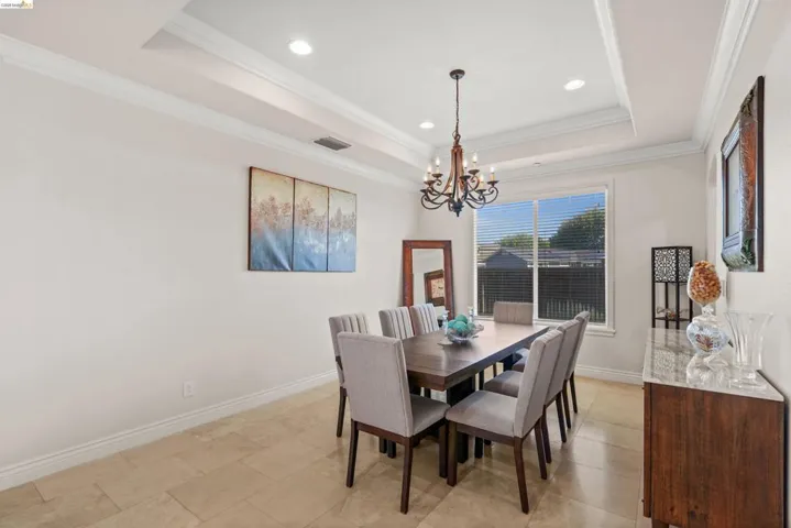 Formal dining space featuring a tray ceiling with recessed lighting and a chandelier, complete with crown molding and baseboards, large window with blinds, and tile flooring