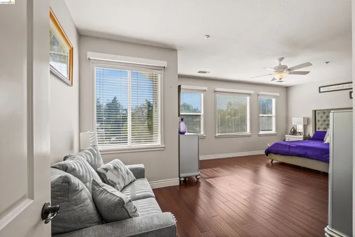 Spacious room featuring rich wood-finish flooring and multiple windows with blinds