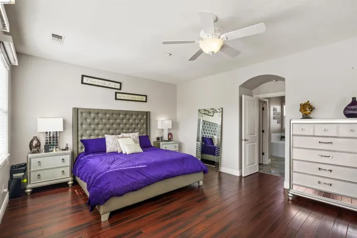 Spacious room featuring rich wood-finish flooring, light neutral-toned walls, and a ceiling fan with integrated lighting