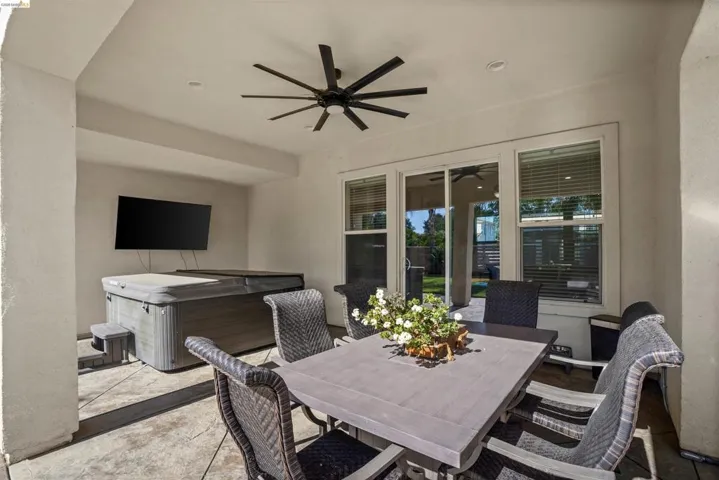 Covered patio featuring a built-in spa, wall-mounted television, and a modern ceiling fan with recessed lighting
