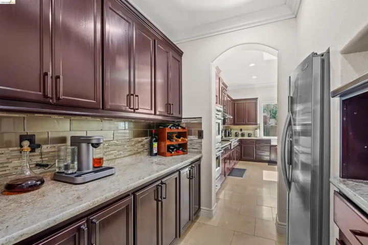 Kitchen featuring extensive dark wood cabinetry, light granite countertops, a mosaic tile backsplash, and stainless steel appliances