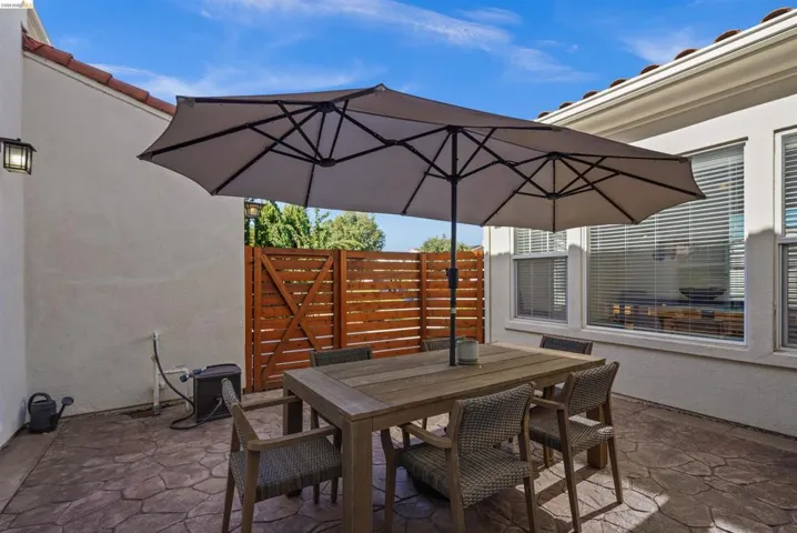 Outdoor patio featuring stamped concrete flooring, stucco exterior walls, a wooden privacy fence, and multiple windows with blinds