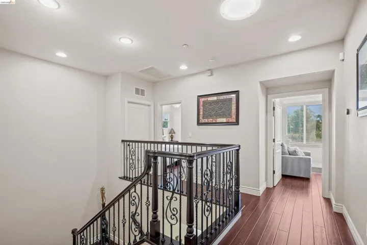 Staircase featuring dark wood newel posts and an ornate wrought iron railing, complemented by wood-finish flooring