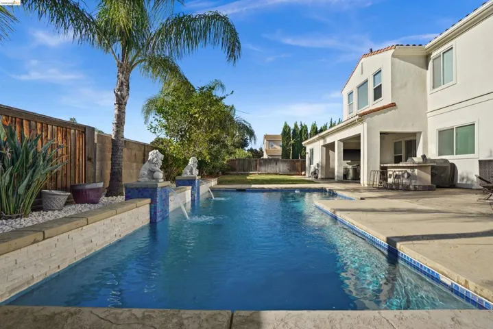 Resort-style backyard featuring a rectangular swimming pool with mosaic tile accents and water features