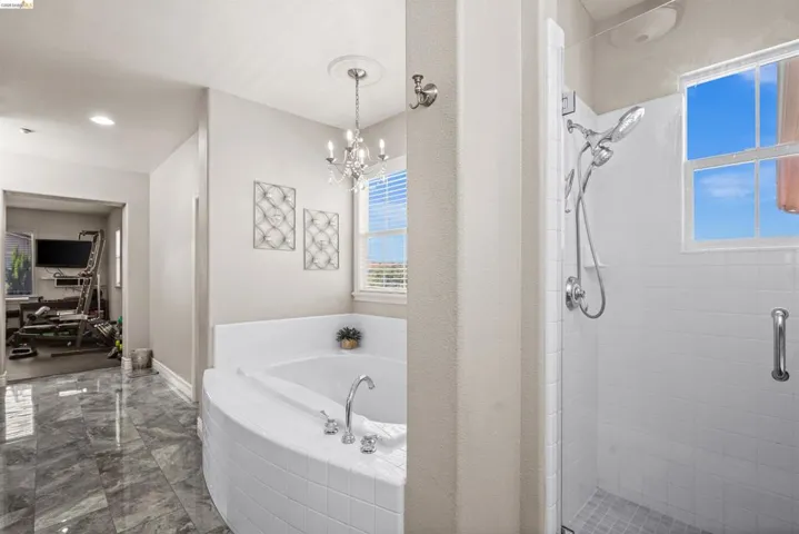 Tile-surround soaking tub with chrome fixtures, accompanied by a separate glass-enclosed shower with subway tile walls and a multi-function showerhead