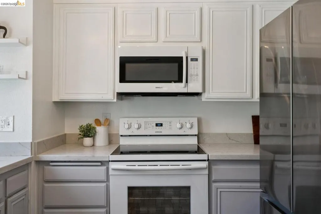 Kitchen features include white upper cabinetry, gray lower cabinetry, light-toned countertops, a white oven/range, and an over-the-range microwave
