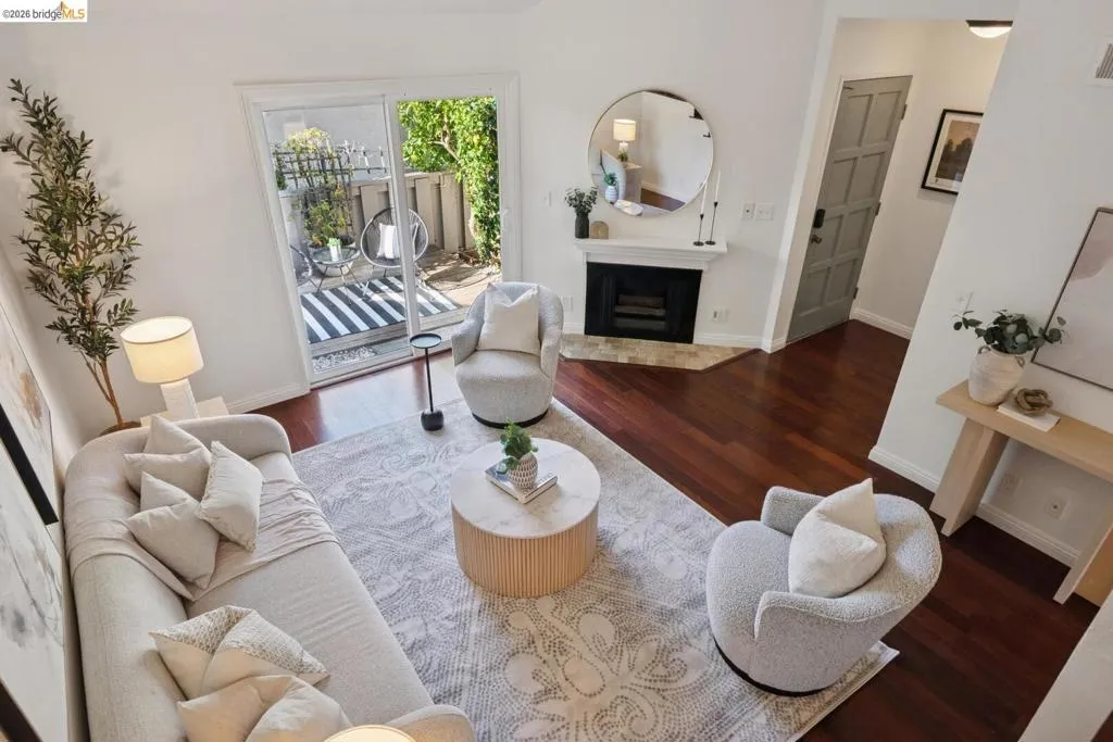 Open-concept living area featuring rich wood-finish flooring, a contemporary fireplace with a white mantel, and a sliding glass door providing access to a private patio