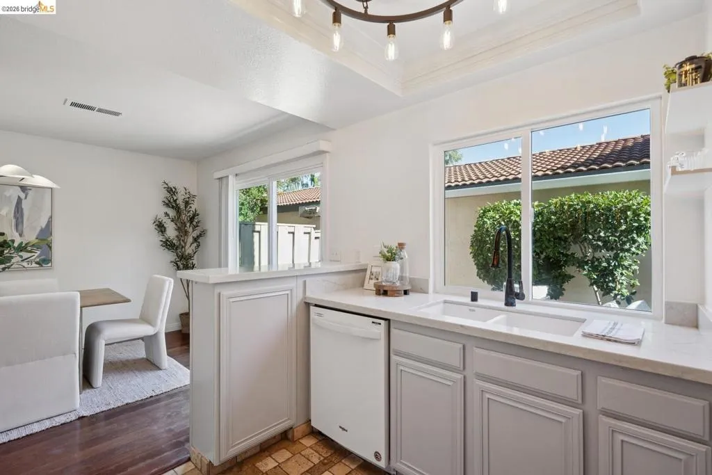 Kitchen featuring white cabinetry, light-toned countertops, an undermount double sink, and a large window above