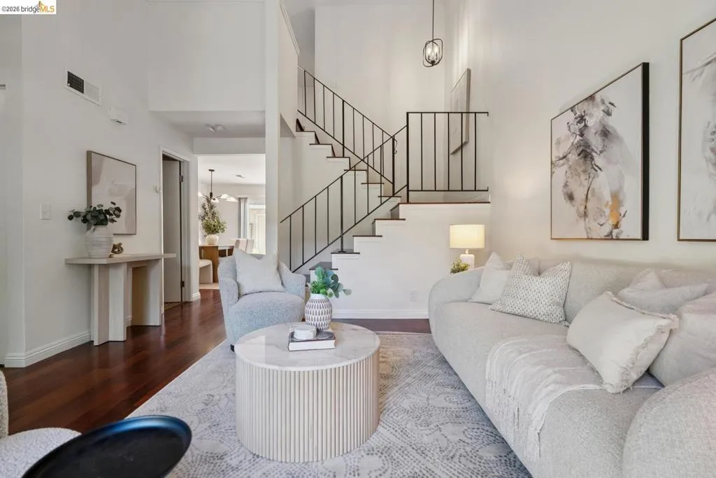 Vaulted ceiling living area featuring rich wood-finish flooring, a contemporary staircase with black metal railings, and a modern hanging light fixture