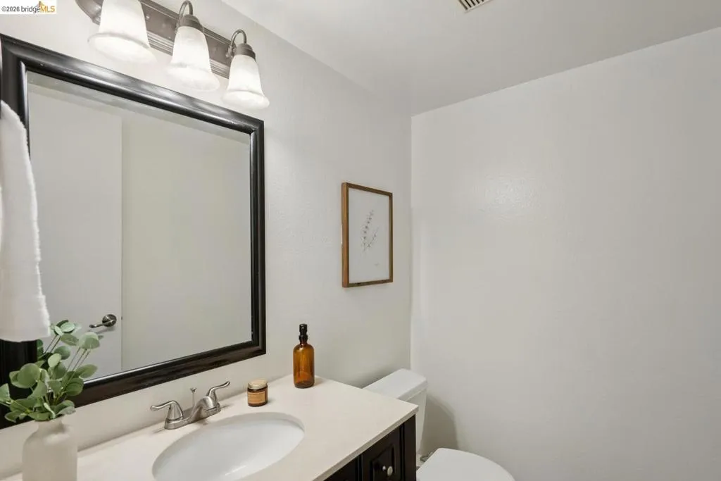 Bathroom featuring a dark wood vanity, light countertop, undermount sink, and a framed mirror with a three-light fixture
