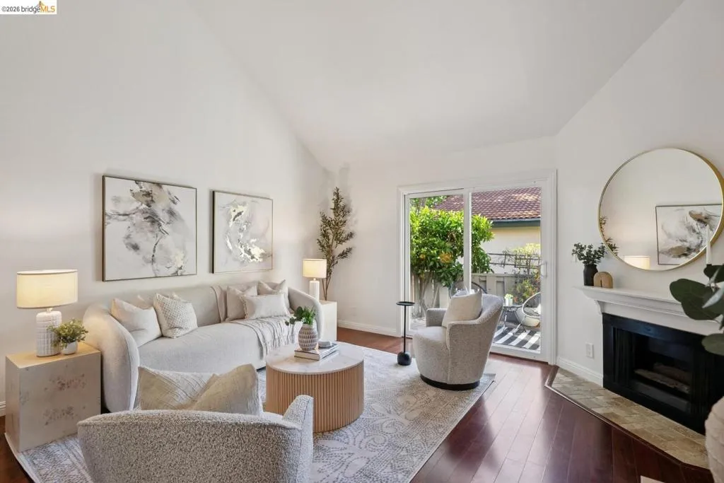 Spacious living area featuring a vaulted ceiling, rich wood-finish flooring, and a fireplace with a stone-tile hearth