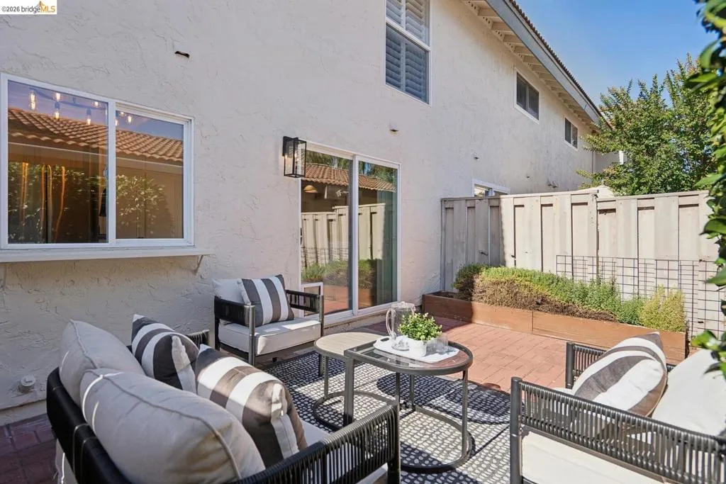 Private brick patio featuring raised planters with established greenery, a sliding glass door for interior access, and an exterior wall lantern