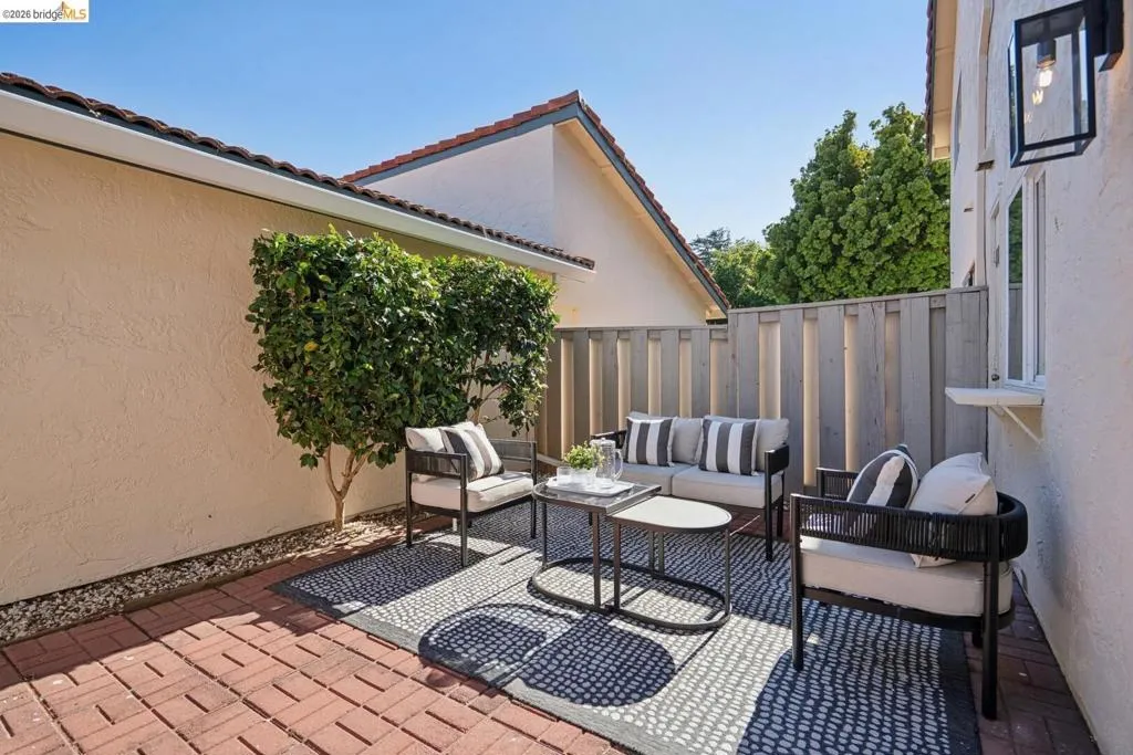 Brick paver patio featuring a privacy fence, stucco exterior, and a contemporary wall light fixture