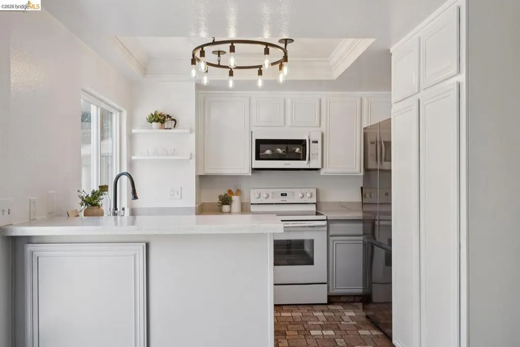 Kitchen featuring white cabinetry, light-toned countertops, a built-in microwave, white electric range, and a dark-finish refrigerator