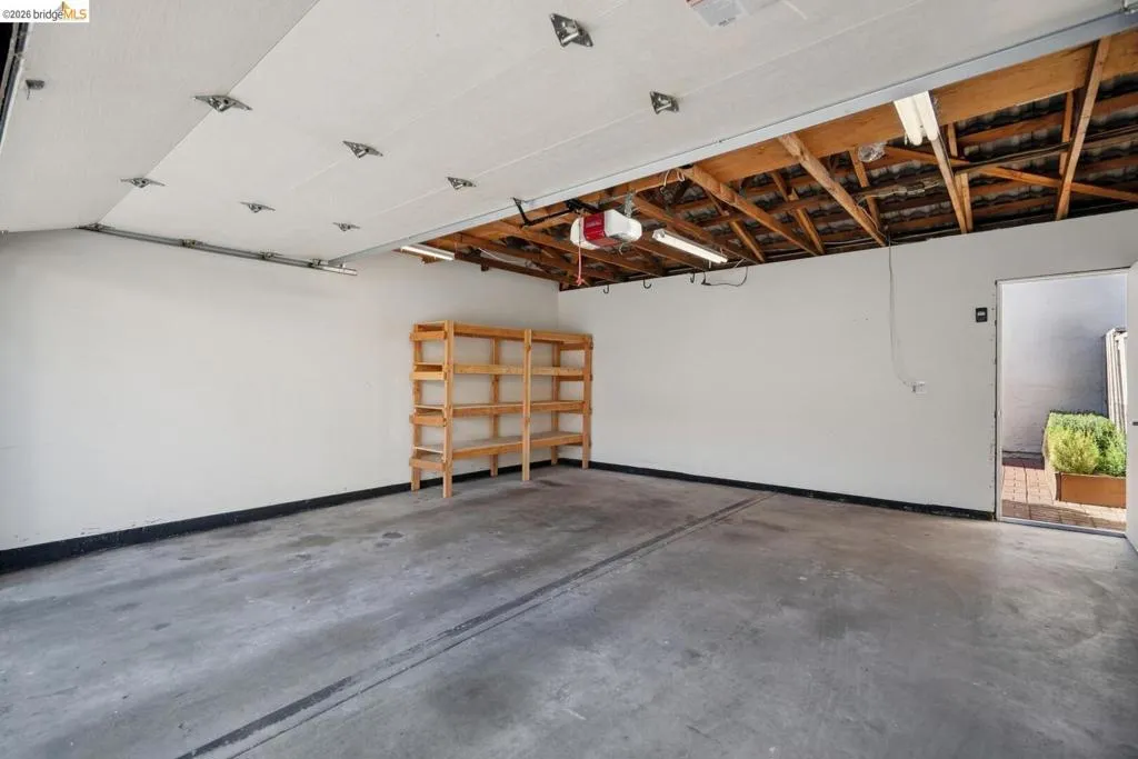 Spacious garage featuring concrete flooring, overhead storage, white walls, and shelving