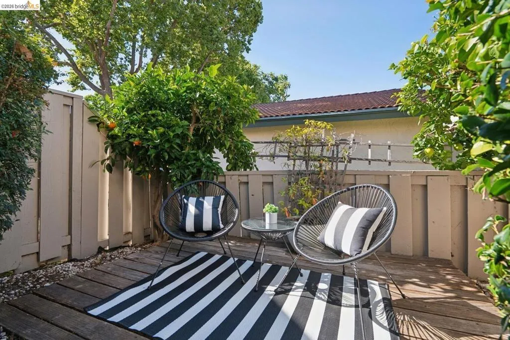 Private outdoor patio featuring wood decking, a privacy fence, and mature citrus trees