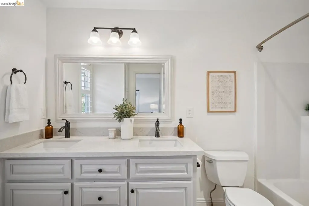 Bright bathroom featuring a dual vanity with light cabinetry and solid surface countertops