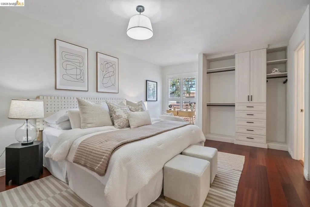 Bedroom featuring rich wood-finish flooring, a contemporary ceiling light fixture, and a window with shutters