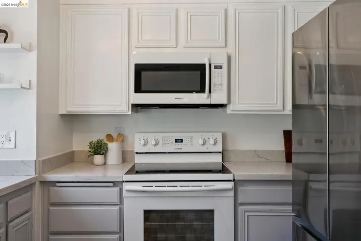 Kitchen features include white upper cabinetry, gray lower cabinetry, light-toned countertops, a white oven/range, and an over-the-range microwave
