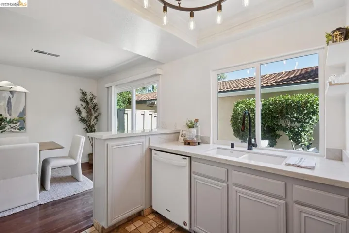 Kitchen featuring white cabinetry, light-toned countertops, an undermount double sink, and a large window above