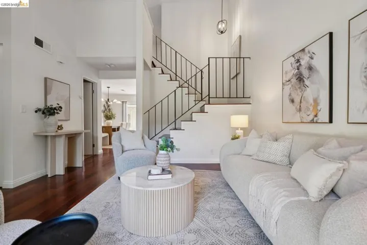 Vaulted ceiling living area featuring rich wood-finish flooring, a contemporary staircase with black metal railings, and a modern hanging light fixture