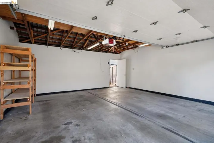 Spacious garage featuring concrete flooring, overhead storage, white walls, and shelving