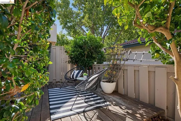 Outdoor patio featuring natural wood decking, a privacy fence, and mature trees providing natural shade