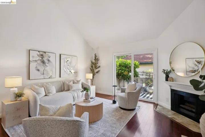 Spacious living area featuring a vaulted ceiling, rich wood-finish flooring, and a fireplace with a stone-tile hearth