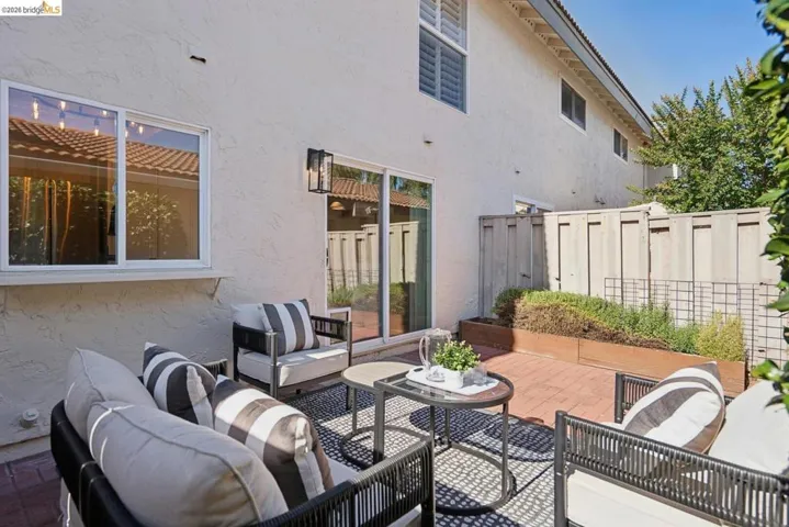 Private brick patio featuring raised planters with established greenery, a sliding glass door for interior access, and an exterior wall lantern