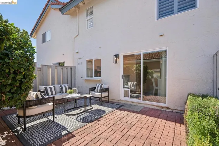 Paved brick patio area featuring a stucco exterior, sliding glass door, and a wall-mounted outdoor light fixture