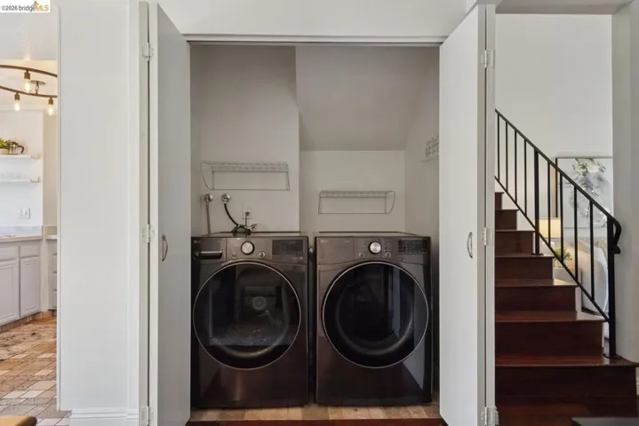 Dedicated laundry closet featuring a front-loading washer and dryer, upper storage shelving, and folding doors